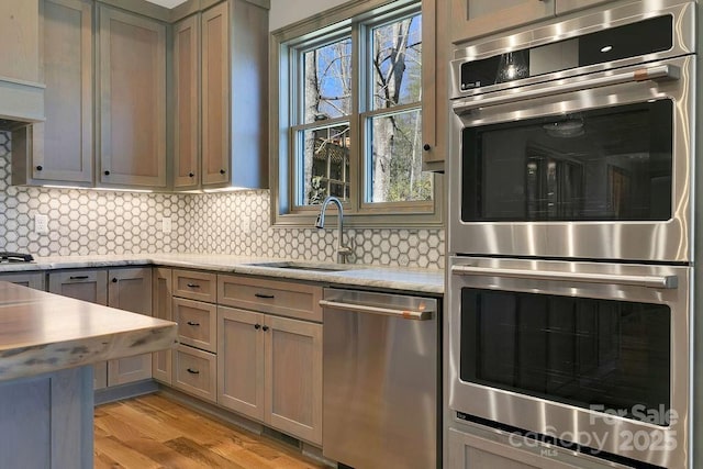 kitchen with stainless steel appliances, a sink, decorative backsplash, light stone countertops, and light wood finished floors