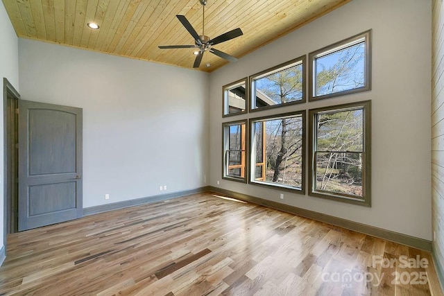 empty room with ceiling fan, a towering ceiling, baseboards, wood ceiling, and light wood-style floors