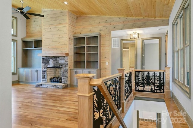 interior space featuring visible vents, wood walls, an upstairs landing, light wood-type flooring, and wooden ceiling