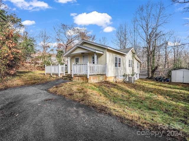 view of front of home featuring a front lawn, a storage unit, a porch, and central AC