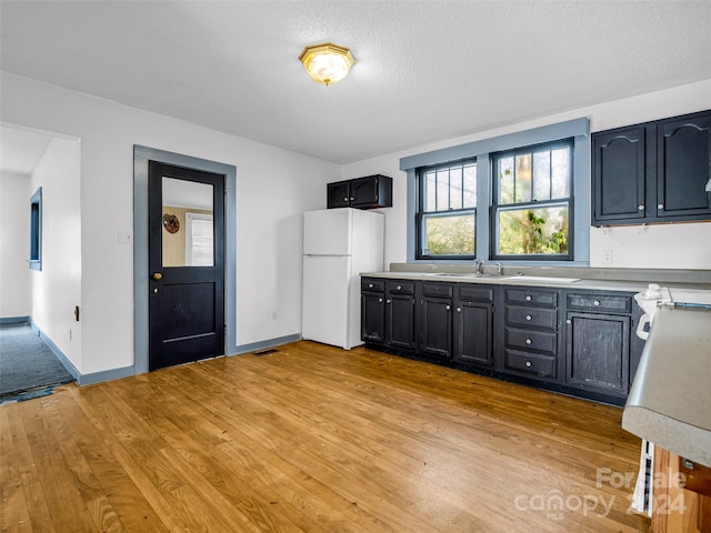 kitchen featuring sink, white fridge, light hardwood / wood-style floors, and a textured ceiling