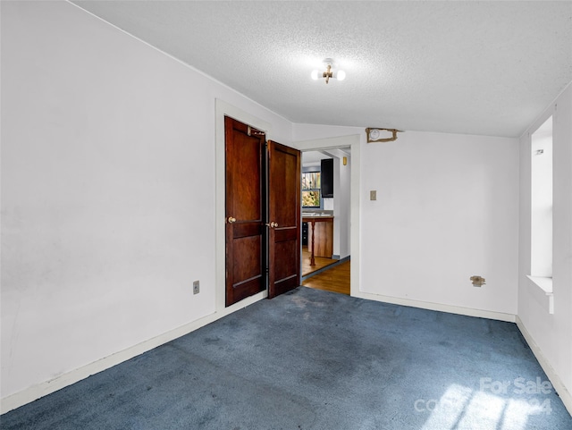 empty room featuring vaulted ceiling, a textured ceiling, and dark colored carpet