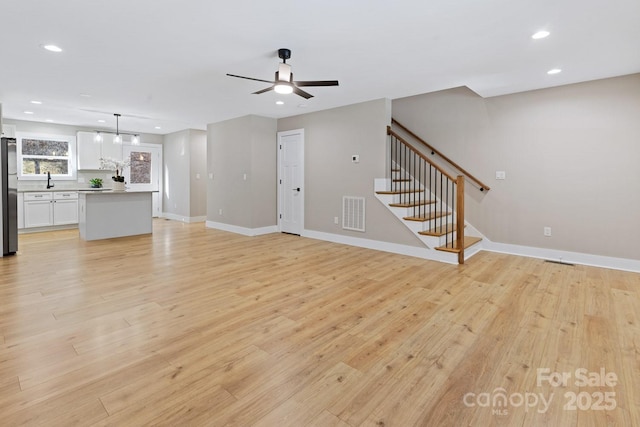 unfurnished living room featuring recessed lighting, stairway, light wood-style floors, ceiling fan, and baseboards