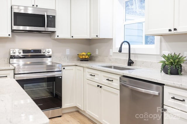 kitchen featuring a sink, white cabinetry, appliances with stainless steel finishes, light stone countertops, and light wood finished floors