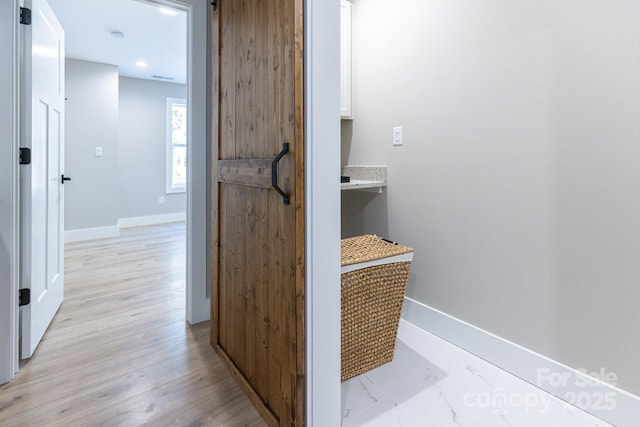 corridor with light wood-type flooring, baseboards, and a barn door