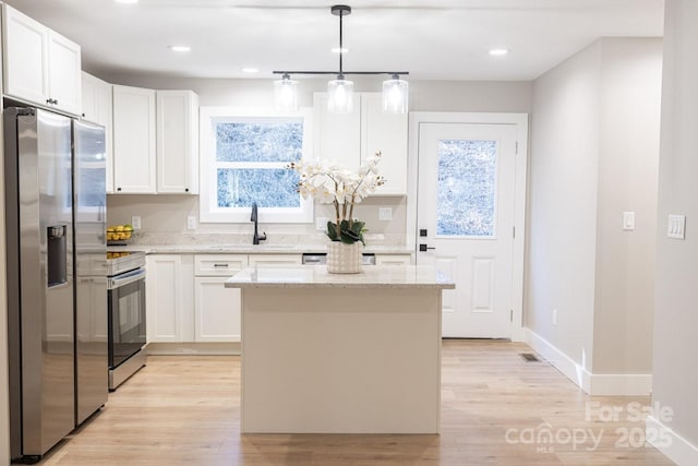 kitchen featuring a kitchen island, white cabinetry, a sink, light wood finished floors, and appliances with stainless steel finishes