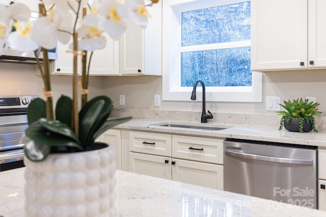 kitchen with stainless steel dishwasher, white cabinets, light stone counters, and a sink