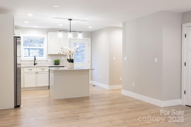 kitchen with a center island, light wood-style flooring, white cabinets, baseboards, and stainless steel refrigerator