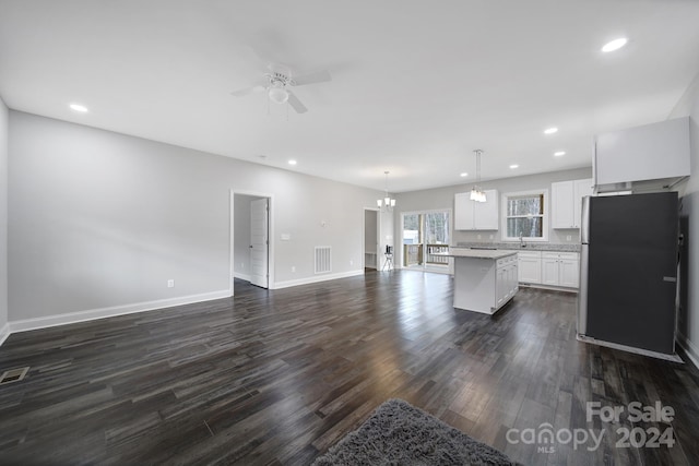 kitchen with stainless steel refrigerator, white cabinetry, dark hardwood / wood-style floors, a kitchen island, and ceiling fan with notable chandelier