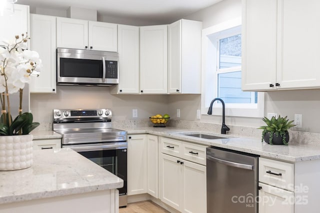 kitchen with appliances with stainless steel finishes, white cabinets, a sink, and light stone countertops