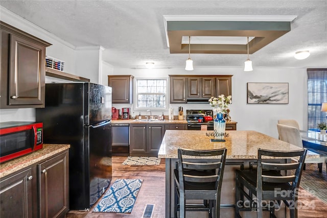 kitchen featuring black appliances, sink, dark hardwood / wood-style floors, light stone counters, and a breakfast bar area