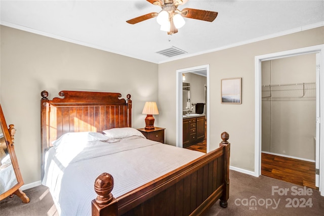 bedroom with dark carpet, a walk in closet, ensuite bath, ceiling fan, and a closet