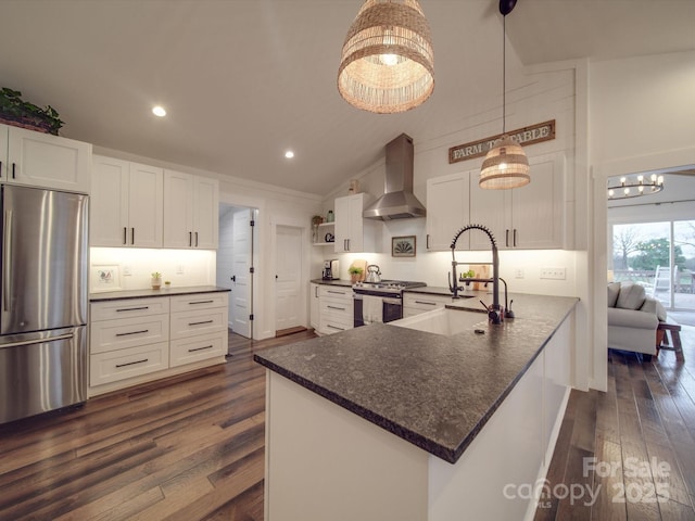 kitchen with sink, wall chimney range hood, kitchen peninsula, white cabinets, and appliances with stainless steel finishes