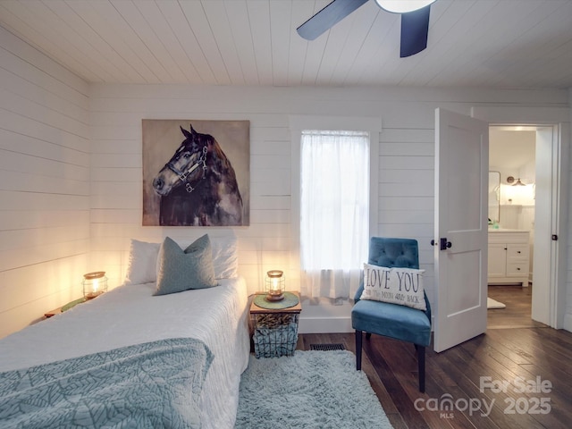 bedroom featuring ceiling fan, dark hardwood / wood-style floors, and wooden walls