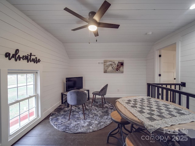 living area with dark hardwood / wood-style floors, vaulted ceiling, ceiling fan, and wooden walls