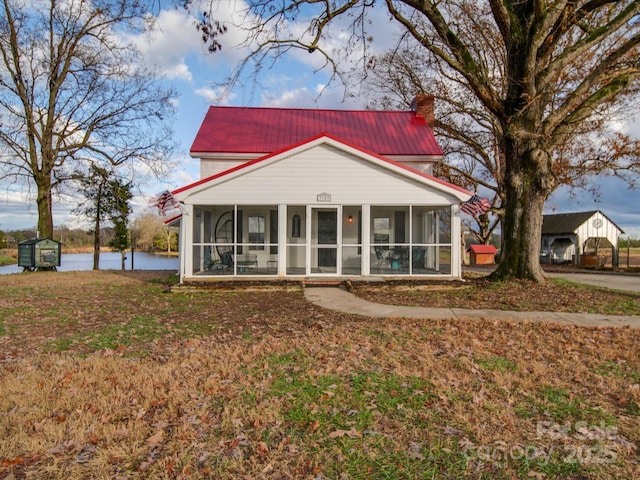 view of front facade featuring a front lawn, a sunroom, and a water view