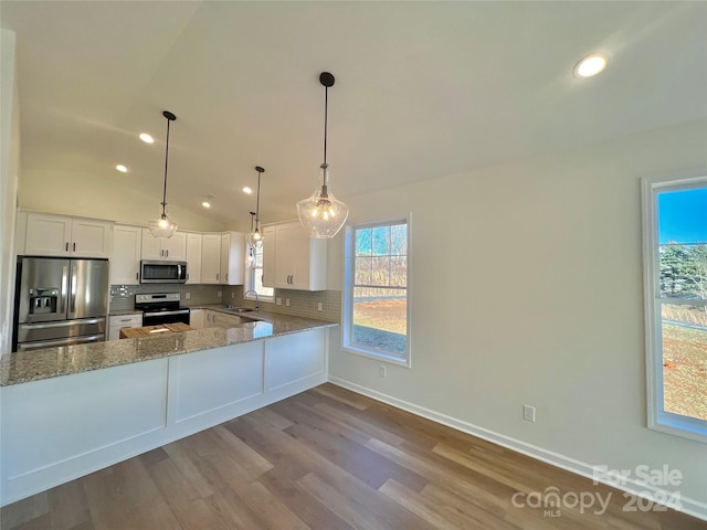 kitchen featuring pendant lighting, lofted ceiling, kitchen peninsula, appliances with stainless steel finishes, and white cabinetry