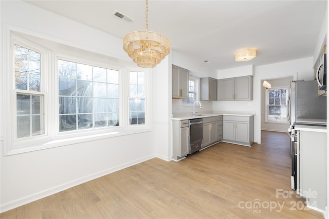 kitchen featuring stainless steel appliances, a notable chandelier, pendant lighting, gray cabinets, and light wood-type flooring