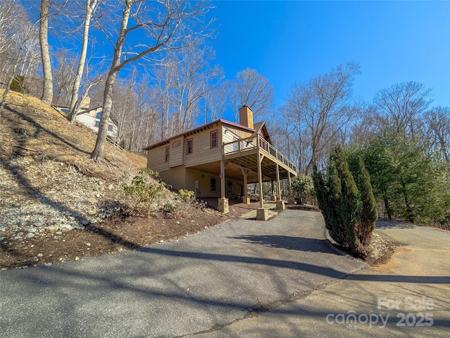 view of front of house featuring driveway, a chimney, and a wooden deck