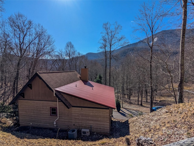 view of side of home with a mountain view, a chimney, a forest view, and central AC unit