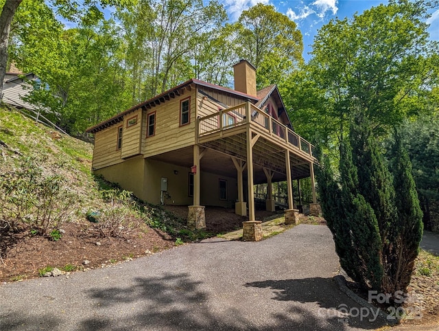 view of property exterior with driveway, a chimney, and a deck