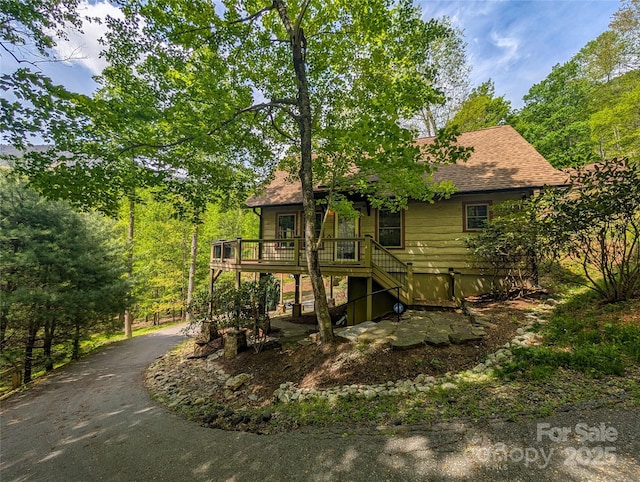 back of property with roof with shingles, a wooden deck, driveway, and stairway