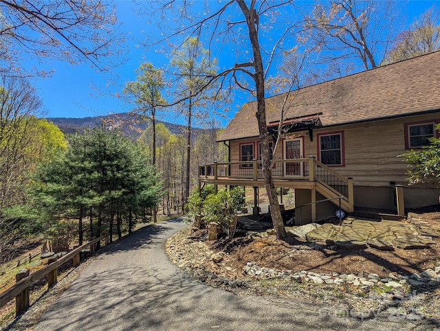 view of side of home with roof with shingles, a deck with mountain view, and stairway