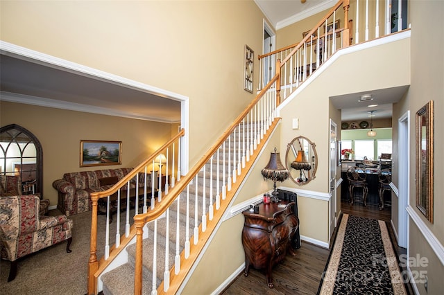 stairway with wood-type flooring, ornamental molding, and a towering ceiling