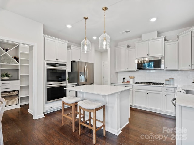 kitchen featuring white cabinets, backsplash, hanging light fixtures, and appliances with stainless steel finishes