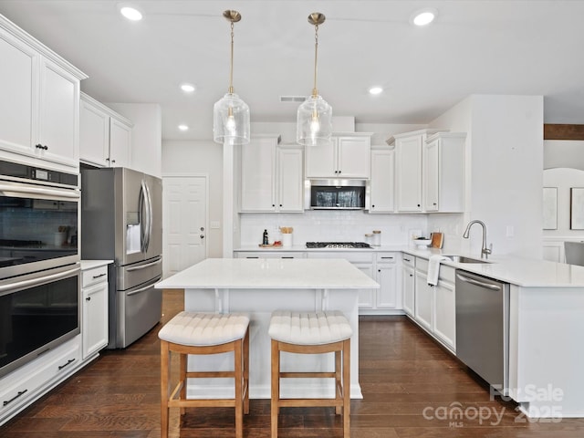 kitchen featuring hanging light fixtures, backsplash, white cabinetry, appliances with stainless steel finishes, and sink