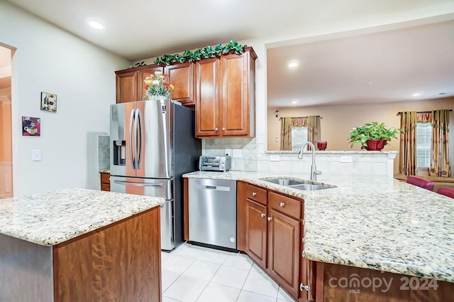 kitchen with light stone countertops, sink, stainless steel appliances, backsplash, and a kitchen island