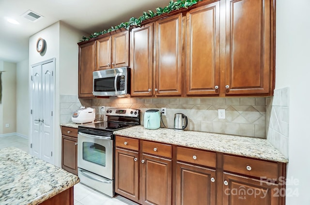 kitchen featuring tasteful backsplash, light stone counters, light tile patterned floors, and appliances with stainless steel finishes