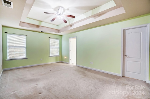 unfurnished room with a raised ceiling, light carpet, and ceiling fan