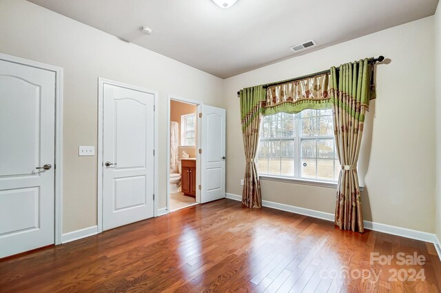 unfurnished bedroom with ensuite bath and wood-type flooring