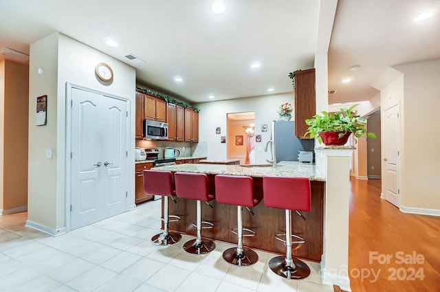 kitchen featuring appliances with stainless steel finishes, light stone counters, a breakfast bar, sink, and light tile patterned floors