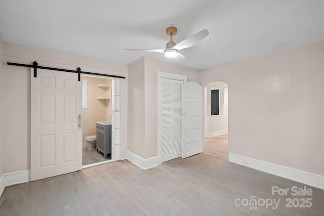 unfurnished bedroom with a closet, a barn door, light hardwood / wood-style flooring, and a textured ceiling