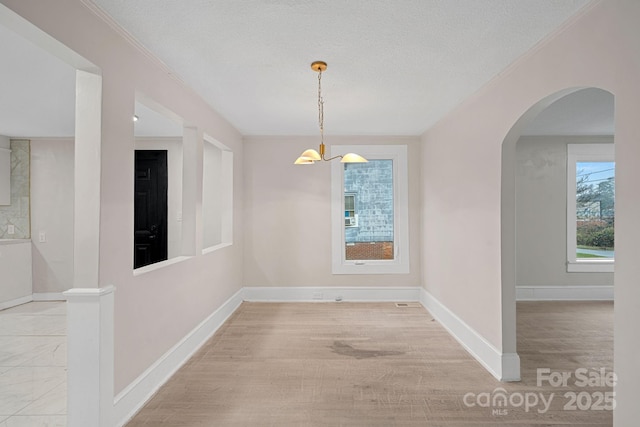 unfurnished dining area with ornamental molding, light hardwood / wood-style floors, and a textured ceiling