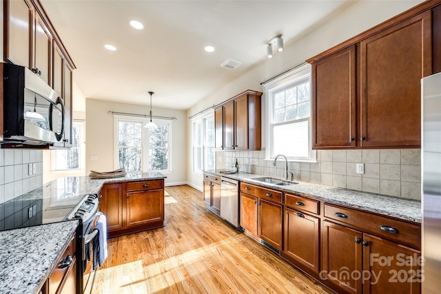 kitchen with light stone countertops, appliances with stainless steel finishes, hanging light fixtures, and sink