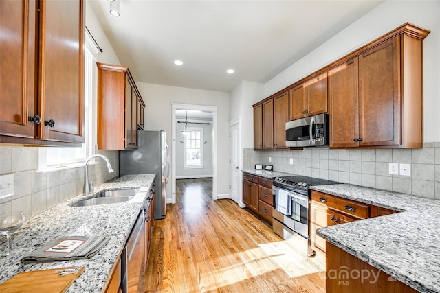 kitchen featuring sink, stainless steel appliances, light stone counters, decorative backsplash, and light wood-type flooring