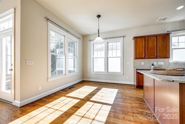 kitchen featuring backsplash, light stone counters, light hardwood / wood-style flooring, and decorative light fixtures