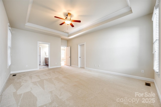 unfurnished bedroom with ceiling fan, a raised ceiling, ensuite bathroom, light colored carpet, and ornamental molding