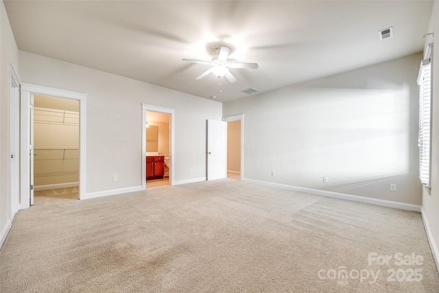 unfurnished bedroom featuring light carpet, ensuite bathroom, ceiling fan, a spacious closet, and a closet