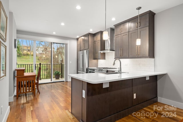 kitchen featuring wall chimney exhaust hood, hanging light fixtures, kitchen peninsula, light hardwood / wood-style floors, and high end fridge