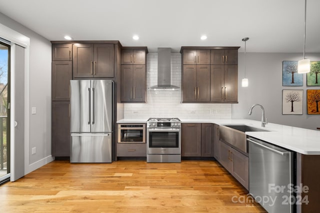 kitchen featuring wall chimney range hood, hanging light fixtures, light hardwood / wood-style flooring, kitchen peninsula, and stainless steel appliances