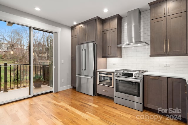 kitchen featuring appliances with stainless steel finishes, light hardwood / wood-style flooring, plenty of natural light, and wall chimney range hood