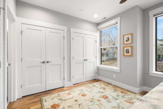 bedroom with multiple windows, multiple closets, ceiling fan, and light hardwood / wood-style floors