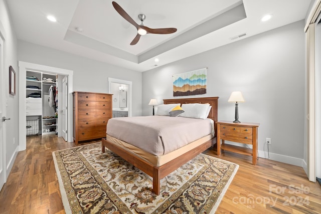 bedroom with a raised ceiling, a walk in closet, ceiling fan, wood-type flooring, and a closet