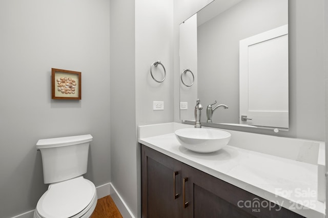 half bath featuring vanity, baseboards, wood finished floors, and toilet