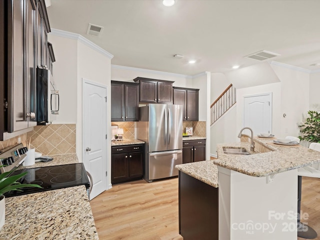 kitchen with light stone countertops, sink, a kitchen breakfast bar, stainless steel fridge, and stove