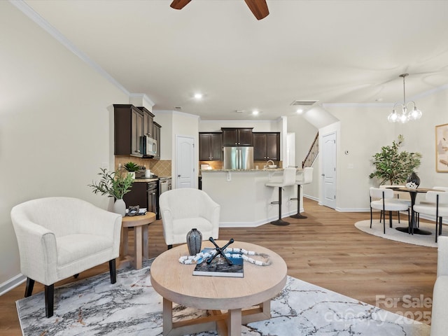 living room with ceiling fan with notable chandelier, ornamental molding, and light hardwood / wood-style flooring